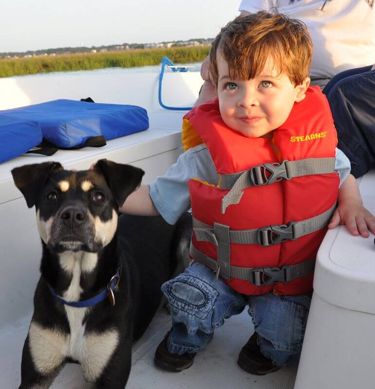 little boy in a lifejacket with a dog on a boat